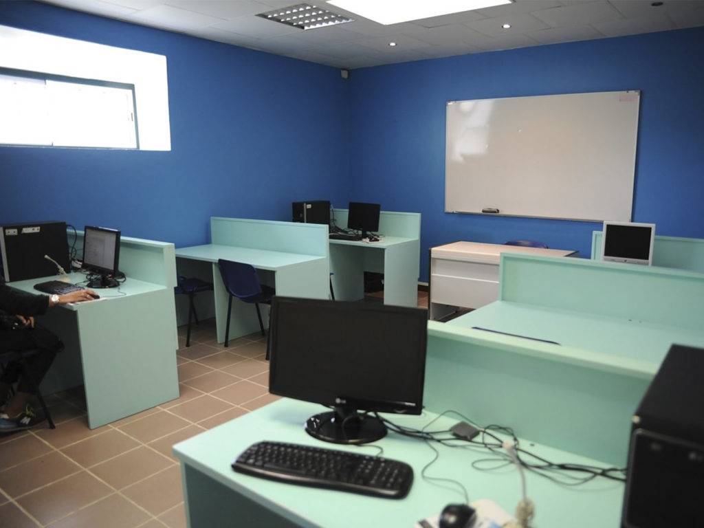 Computer room with blue walls and a window, containing several desks, keyboards, and screens